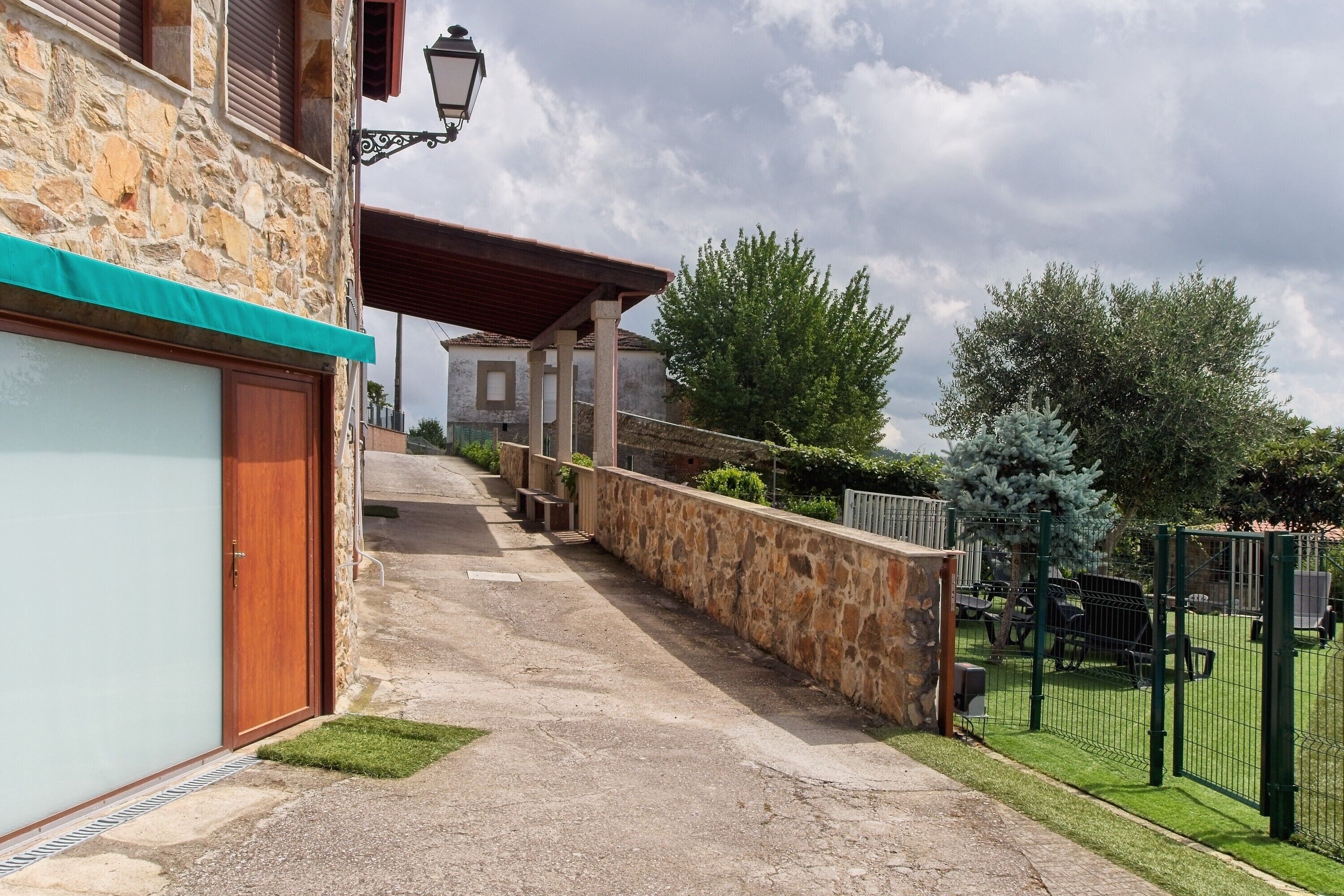 Un bâtiment en pierre doté d’un garage, d’un chemin pavé et d’une zone clôturée agrémentée de verdure.