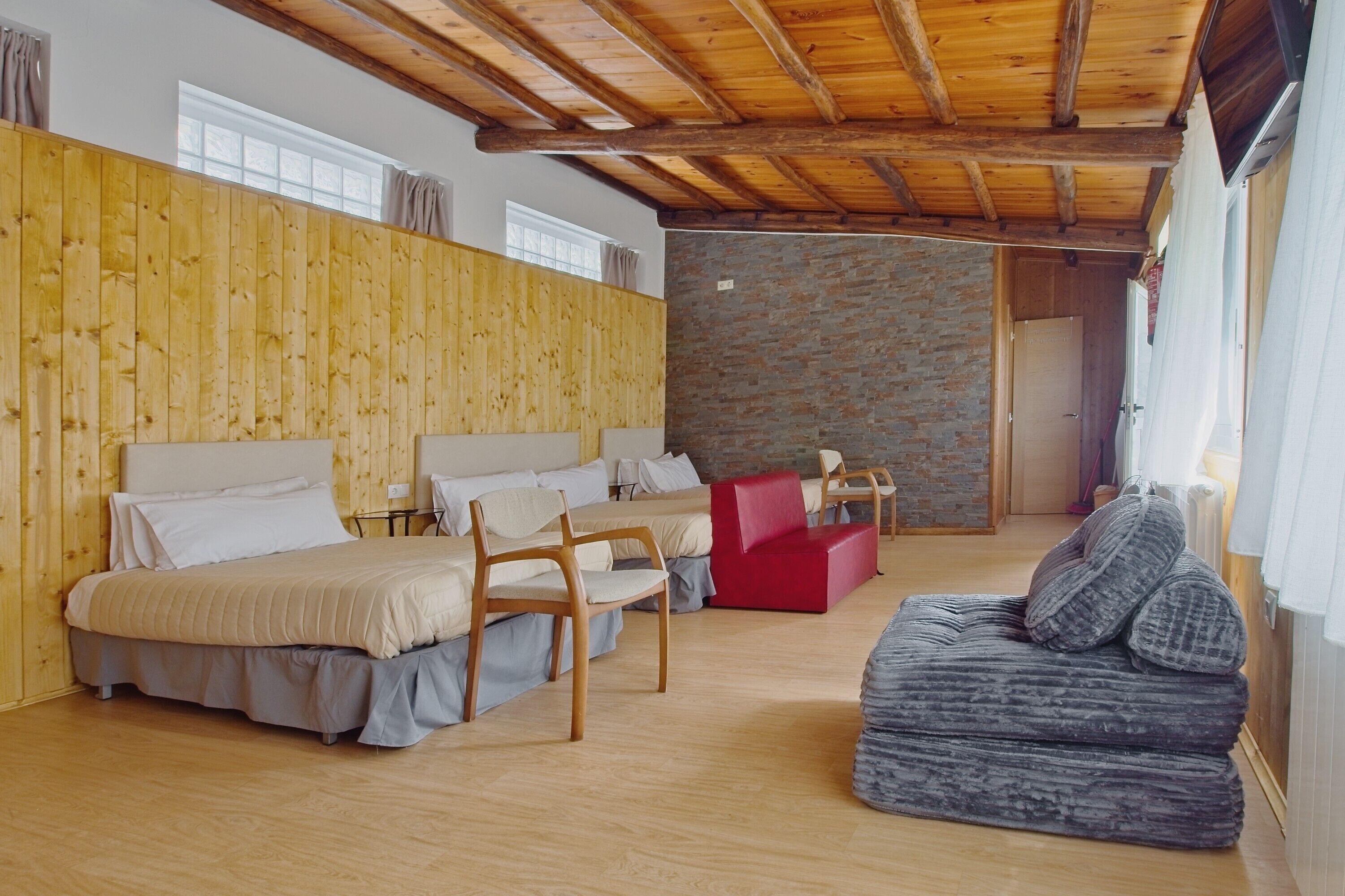Une pièce avec un plafond en bois, un mur en pierre et un lit doté d’une tête de lit rouge. On y trouve deux chaises en bois et un canapé rouge.