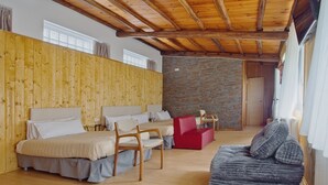 Una habitación con techo de madera, pared de piedra y cama con cabecera roja. Hay dos sillas de madera y un sofá rojo.