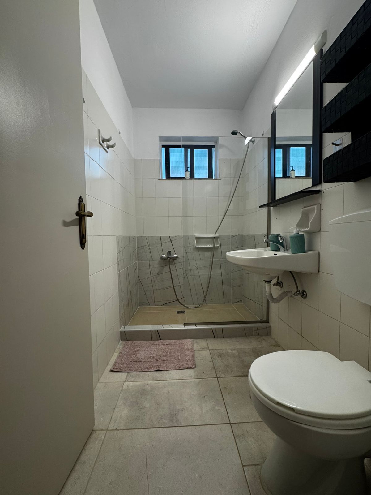 A bathroom with a toilet, sink, shower, and a window.