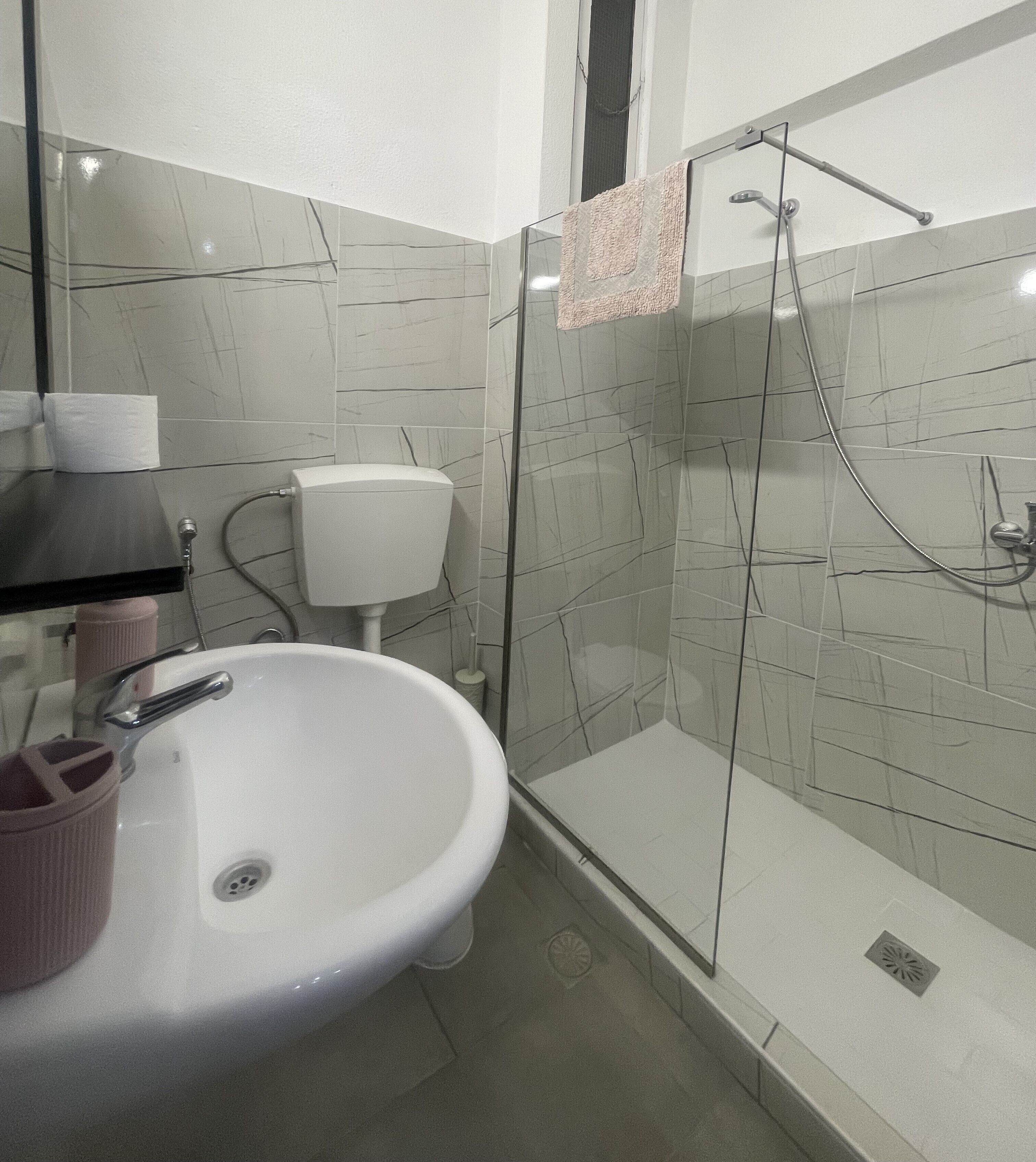 Un baño con lavamanos blanco, inodoro y ducha con mampara de cristal.