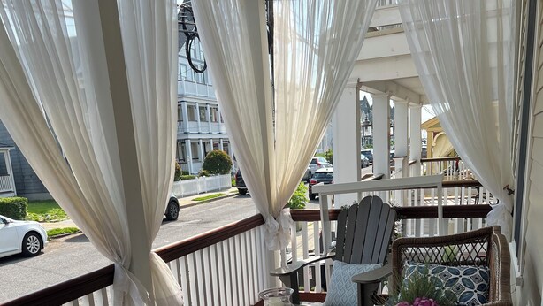 A covered outdoor seating area with wicker furniture, a glass table with a candle, and a decorative vase with flowers.