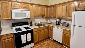 A kitchen with wooden cabinets, a stove, microwave, dishwasher, and a ceiling fan.