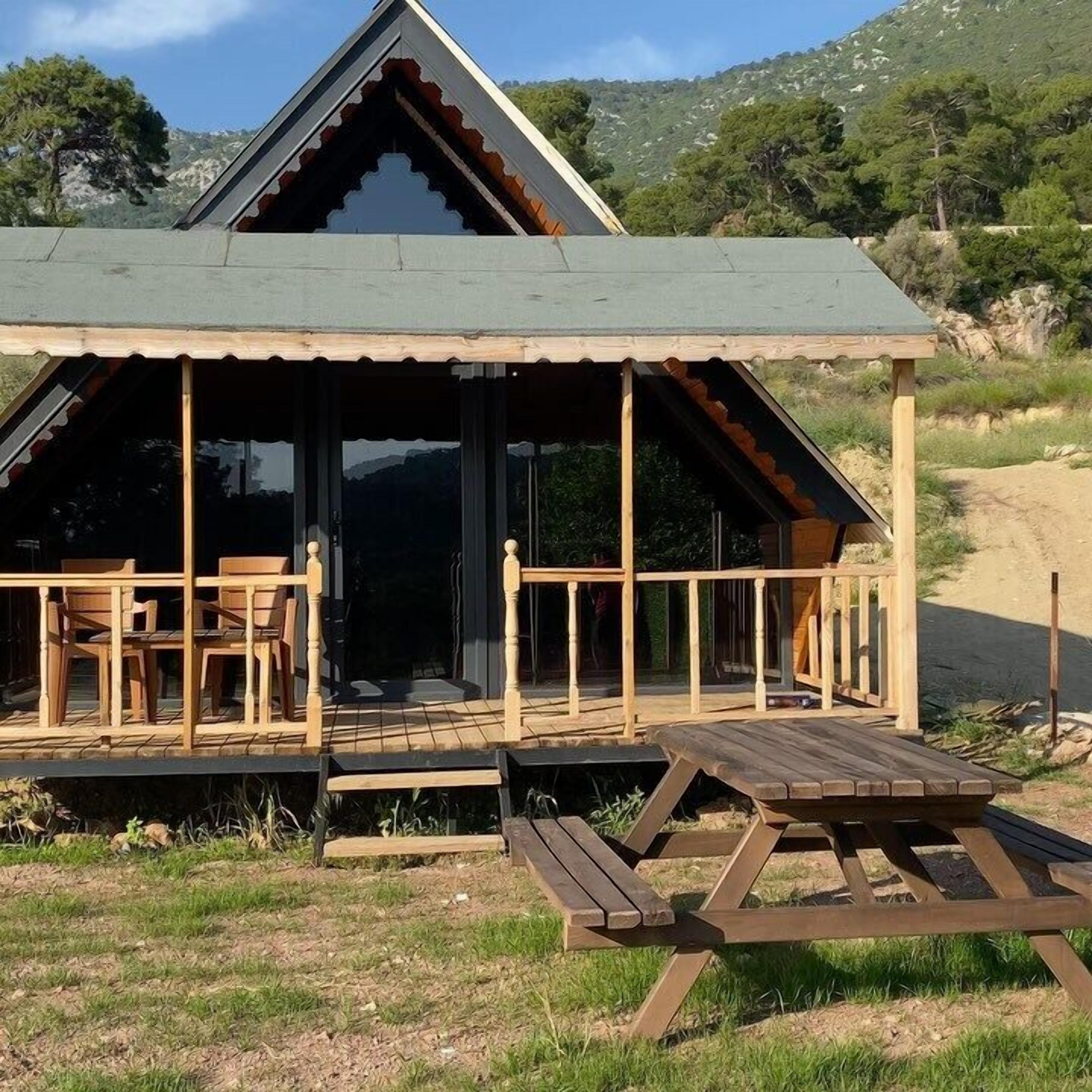 Una cabaña con porche cubierto, mobiliario de madera y una mesa de picnic.