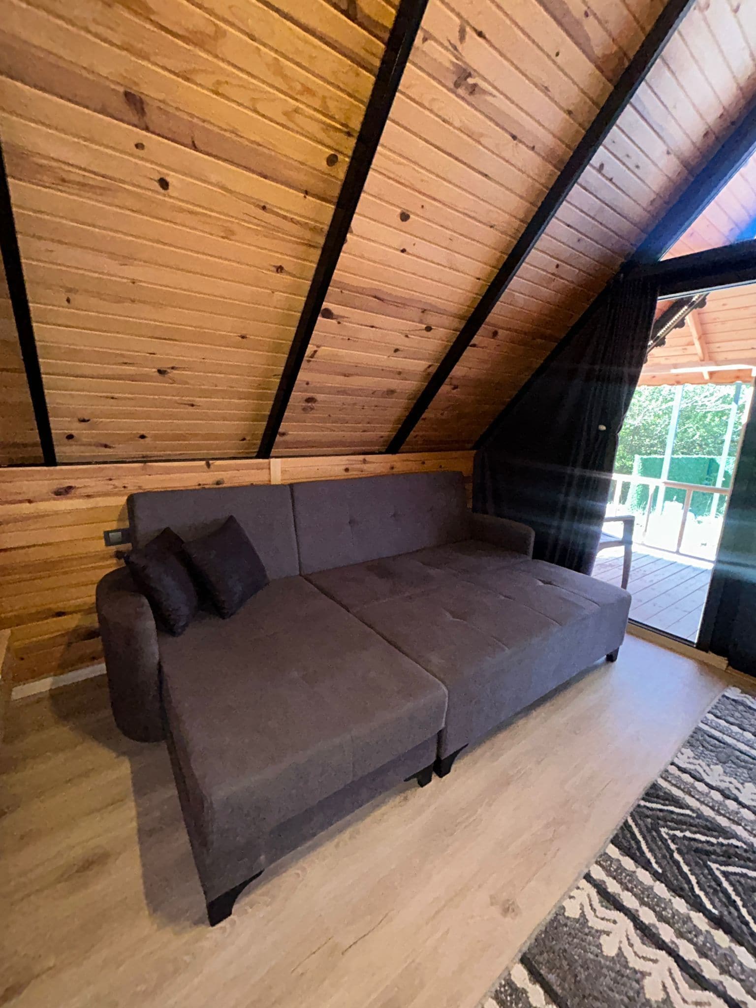 A cozy room with a wooden sloped ceiling, a gray sofa, and a patterned rug.