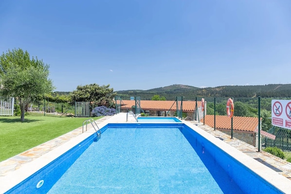 Une piscine rectangulaire à l’eau d’un bleu limpide, entourée d’une terrasse en pierre et en béton.