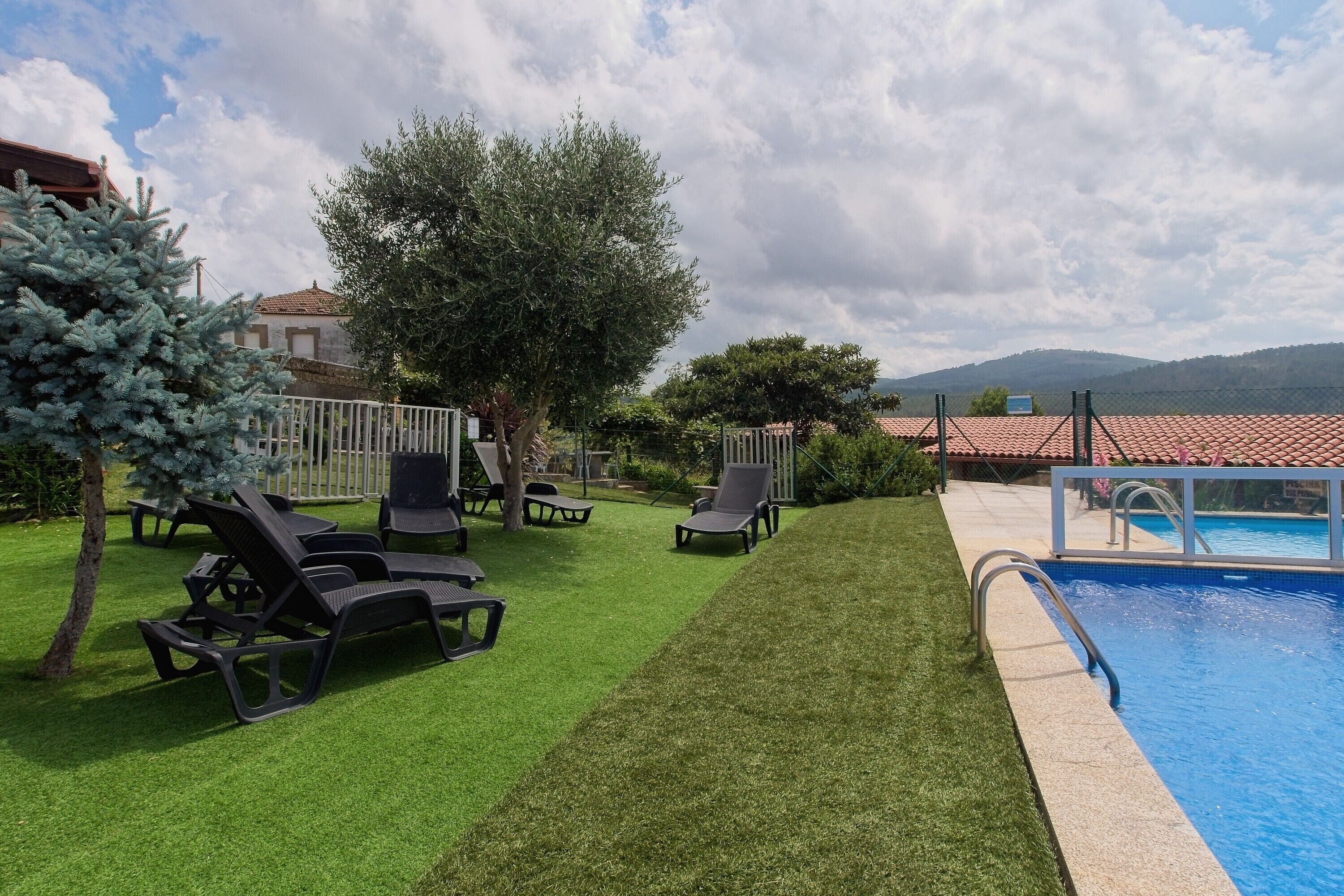 Zona junto a la piscina con césped artificial, sillones de descanso y una piscina.
