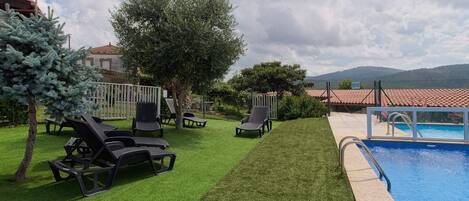 Zona junto a la piscina con césped artificial, sillones de descanso y una piscina.
