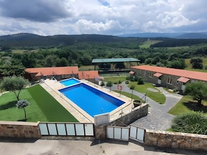 Un espace piscine agrémenté d’un mur en pierre, d’un bâtiment à toit rouge et offrant une vue sur le paysage environnant.
