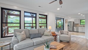 Un salon spacieux avec un canapé gris, une table basse en bois et de grandes fenêtres donnant sur l’extérieur.
