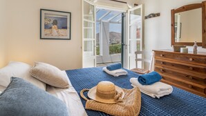 Un dormitorio con cama, cómoda, espejo, un cuadro en la pared y puerta que da a un balcón.