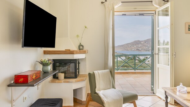 Una habitación con televisión de pantalla plana, chimenea, una silla, una mesa y un balcón con vistas.