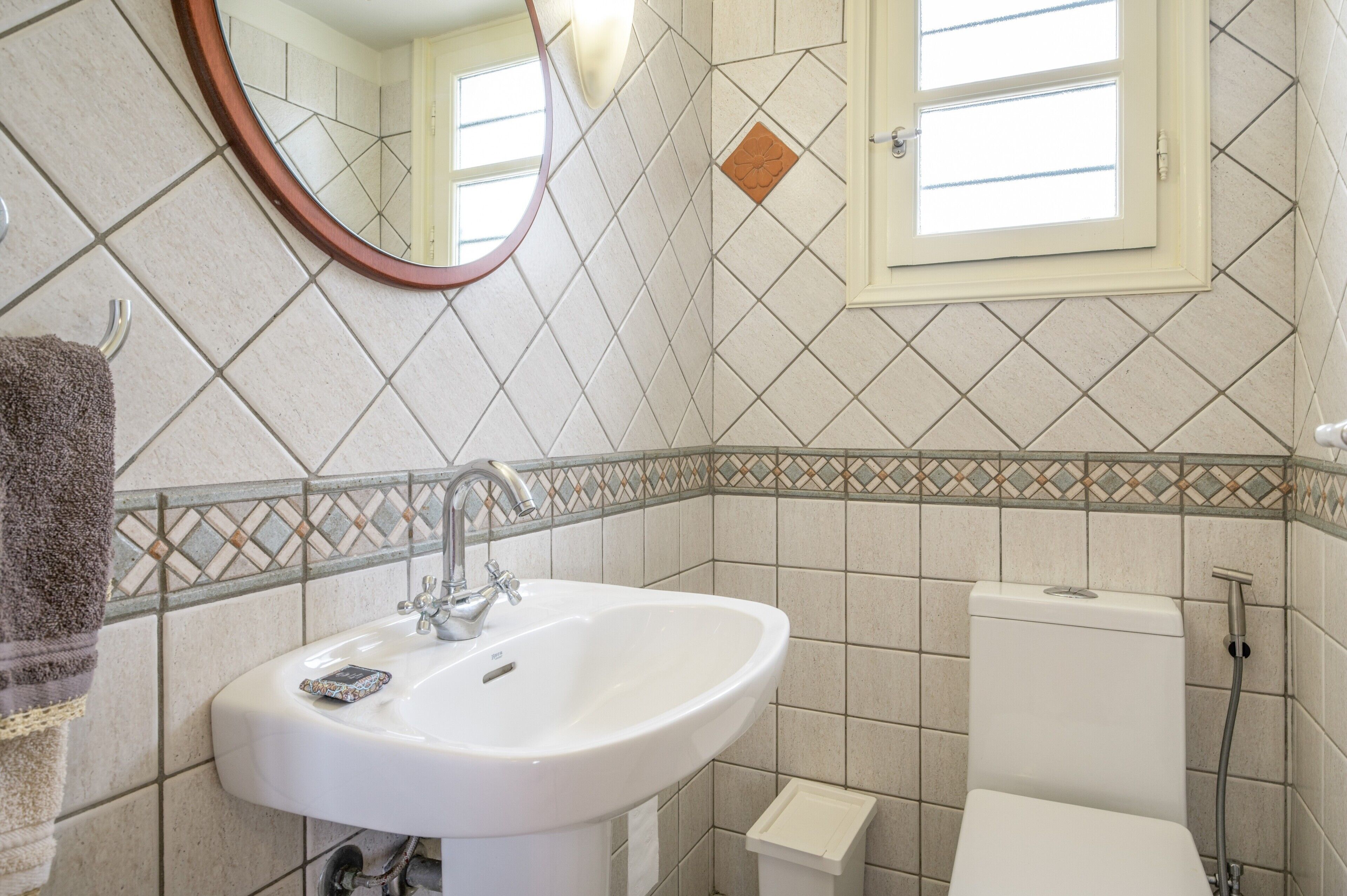 Ein Badezimmer mit weißem Waschbecken, Spiegel, Toilette und Fenster.