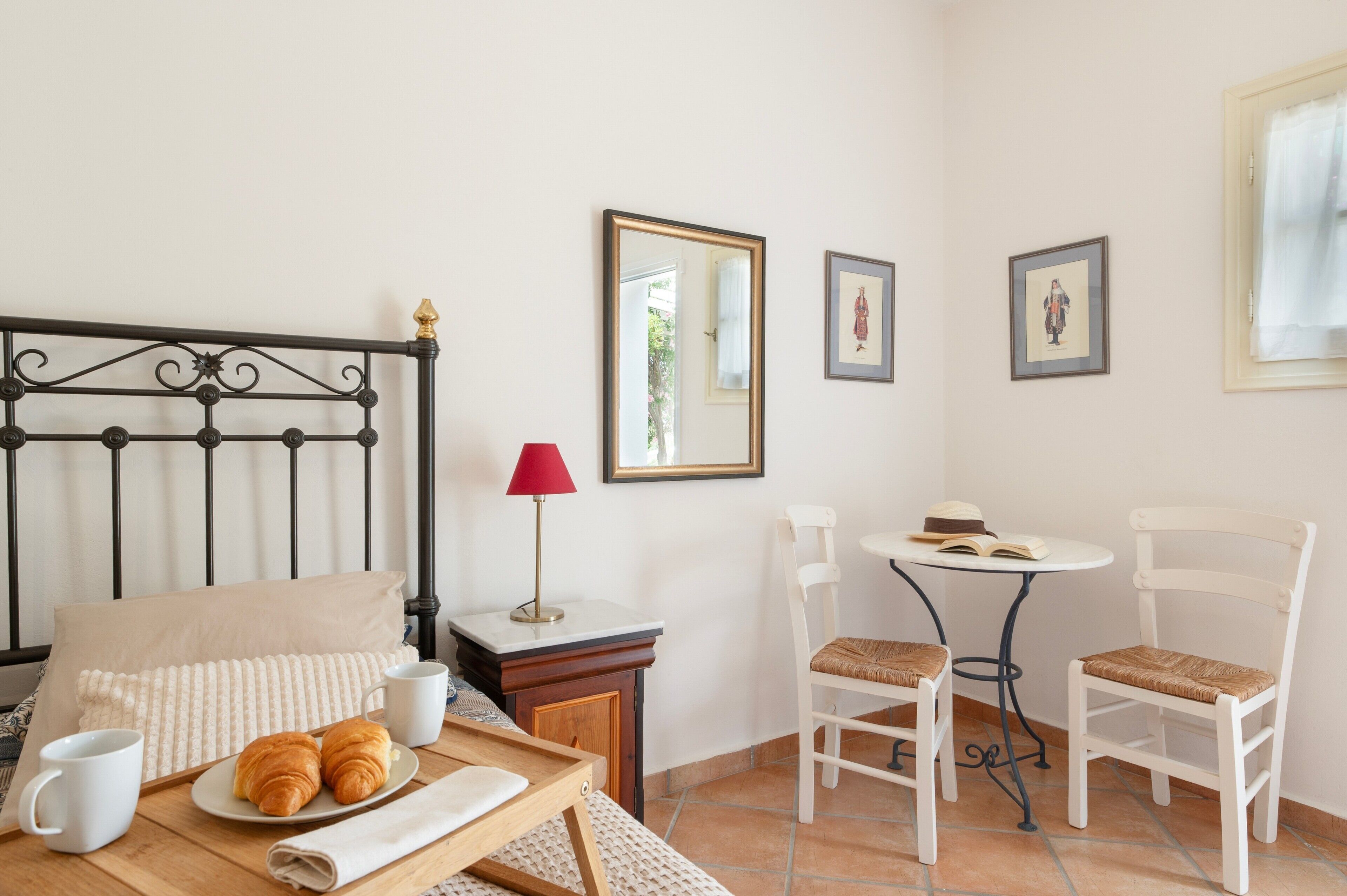 Quarto com cama, mesa de cabeceira, abajur e disposição para café da manhã, incluindo croissants e café.