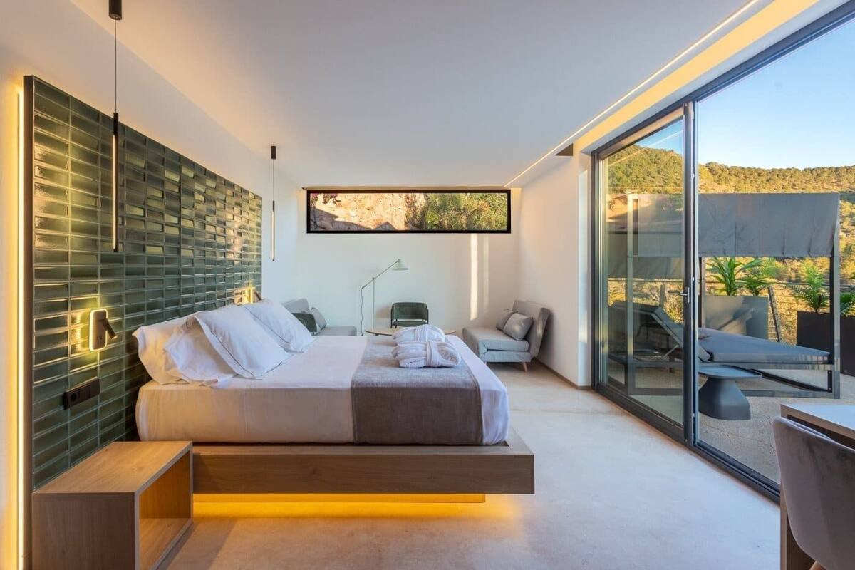 Un dormitorio moderno con cama, mesitas de noche, un escritorio y un ventanal con vistas al exterior.