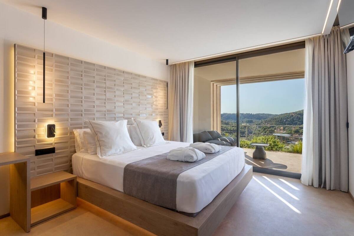 Un dormitorio moderno con una cama grande, una mesita de noche, una lámpara de pared y vistas al exterior.