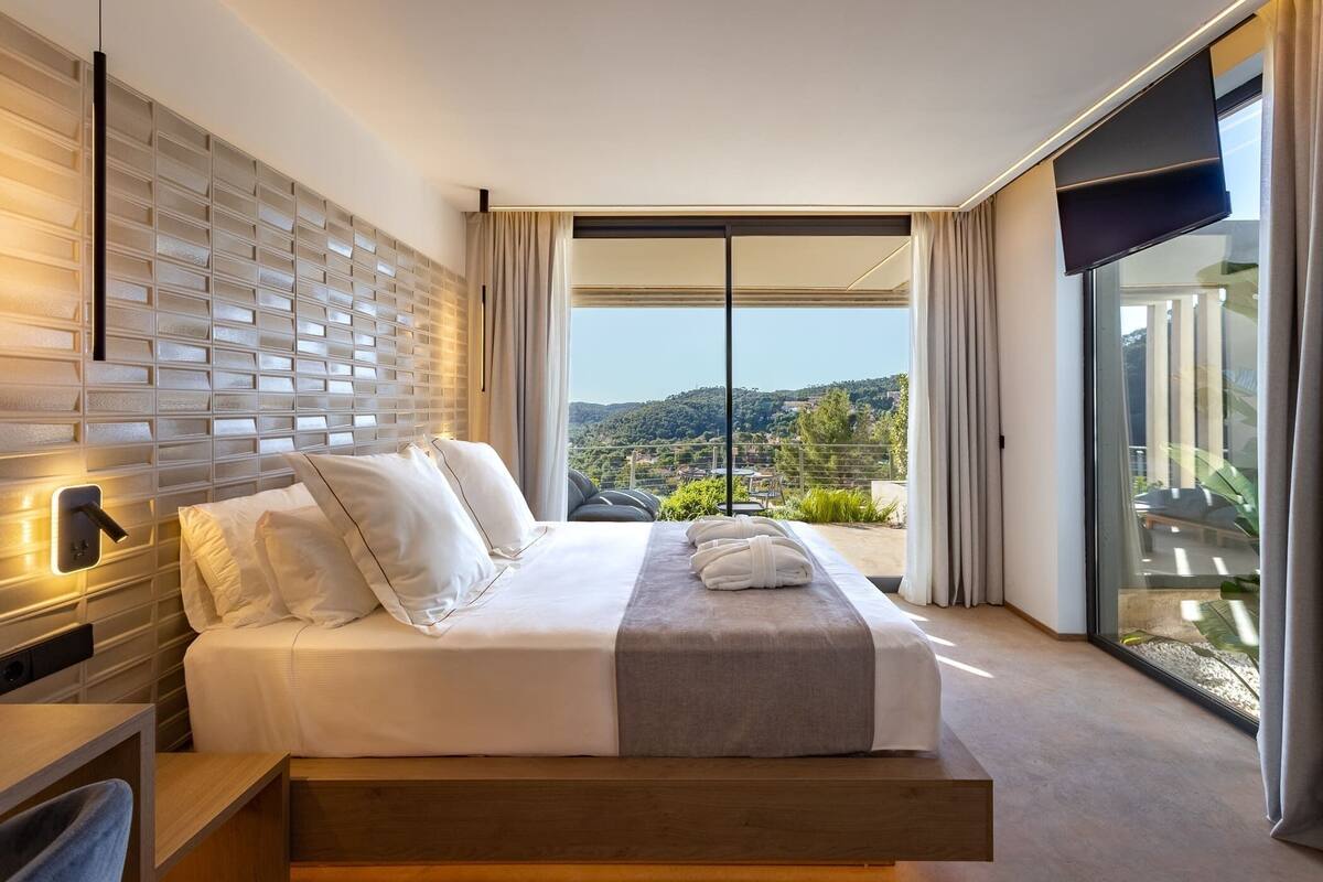 Una habitación de hotel moderna con una cama grande, televisión integrada y balcón con vistas panorámicas.