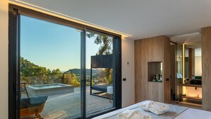 Een moderne slaapkamer met een grote schuifglazen deur naar een terras buiten, inclusief een jacuzzi en zitplaatsen.
