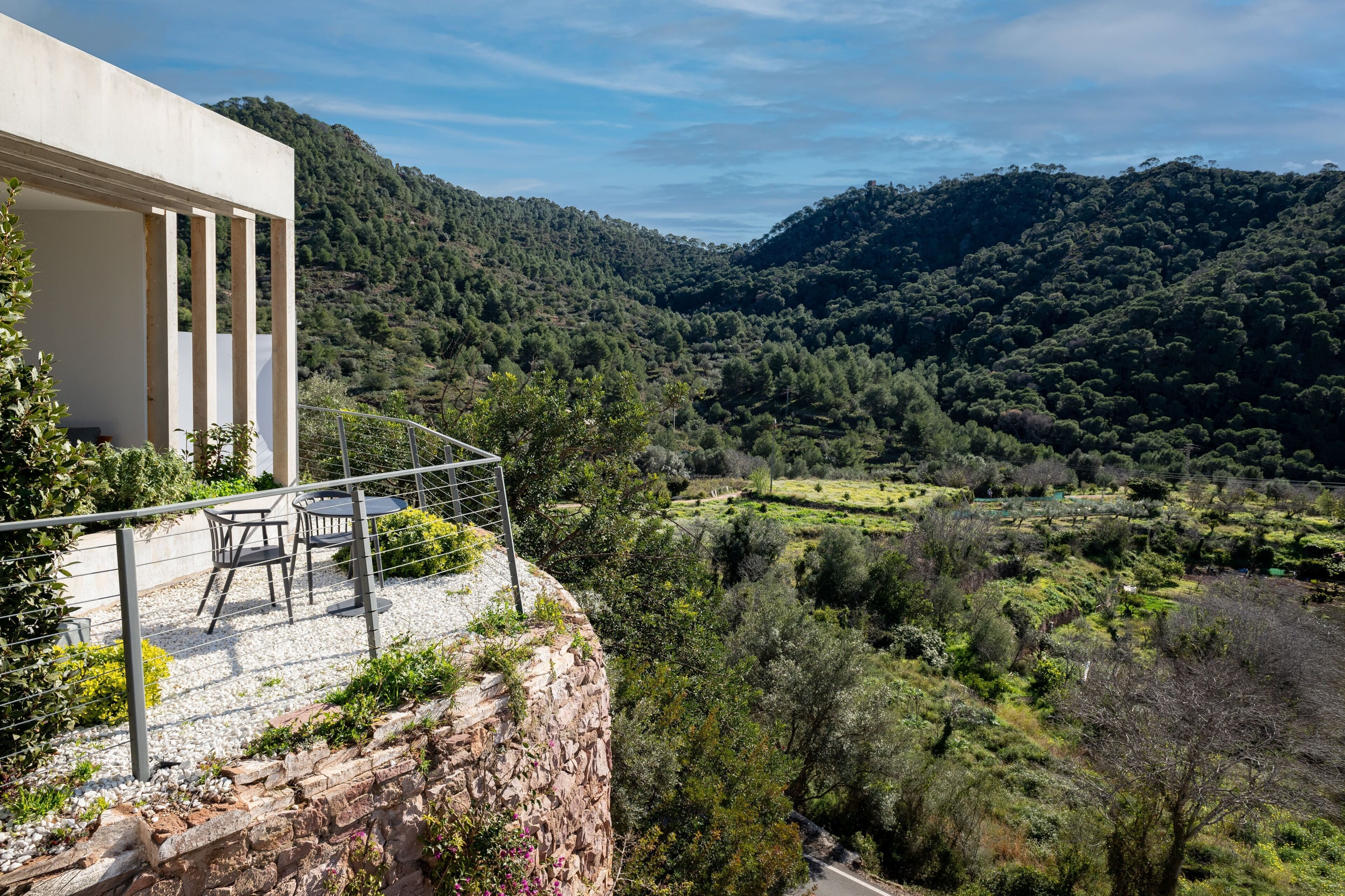 A balcony with a table and chairs overlooking a mountainous landscape.