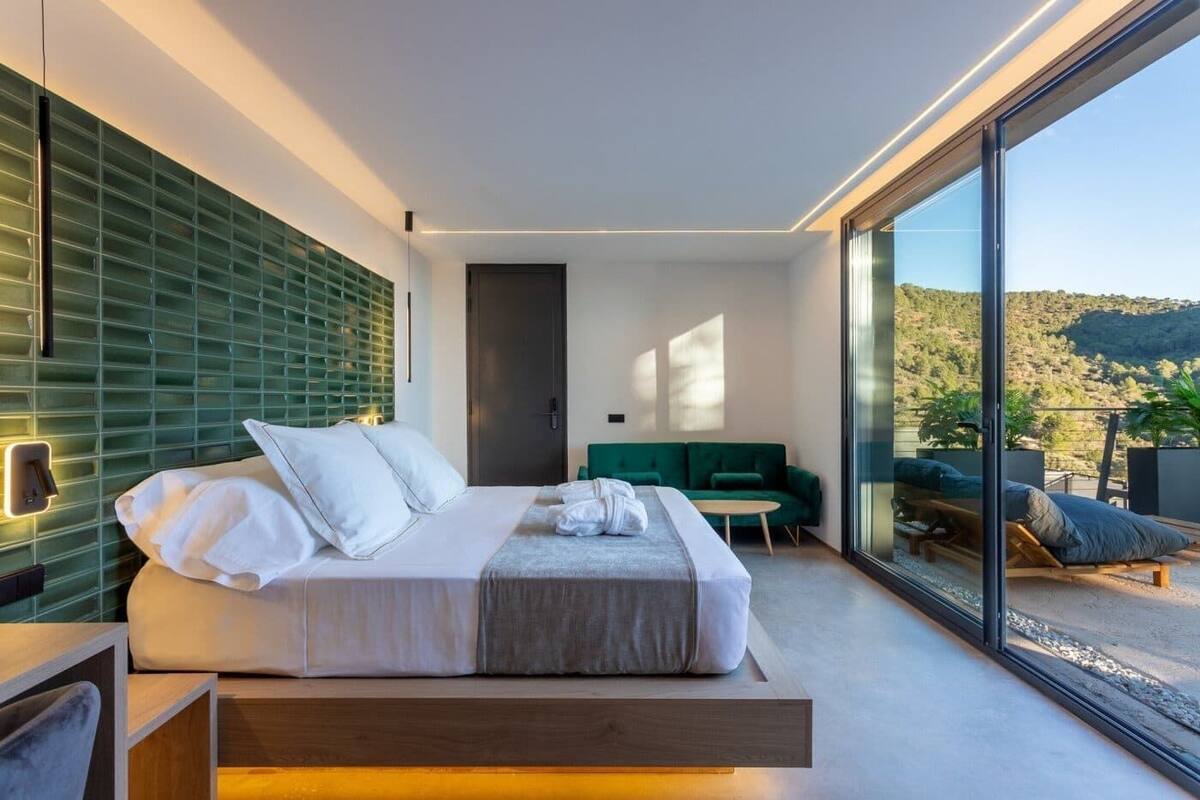 Un dormitorio moderno con una cama, un sofá verde y un amplio ventanal corredera que da a un espacio exterior.