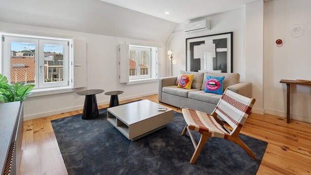 A modern living room with a grey sofa, two black tables, a wooden coffee table, and a patterned armchair.