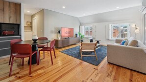 A modern living room with a dining area, a flat-screen TV, and a kitchen with a toaster.