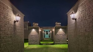A courtyard with a green lawn, stone walls, and a door leading to a building. - FF21-Pods (Bengaluru)