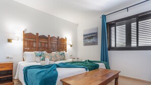 A bedroom with a bed, bedside tables, a wooden headboard, a window with blinds, and a painting on the wall. - Vacation 'Vista Lobos' with Sea View, Shared Pool and Wi-Fi (Corralejo)
