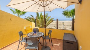A patio with a table, chairs, a large umbrella, and a view of the beach. - Vacation 'Vista Lobos' with Sea View, Shared Pool and Wi-Fi (Corralejo)