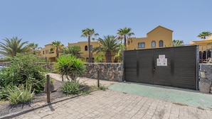 A gated area with a paved walkway, palm trees, and a stone wall. - Vacation 'Vista Lobos' with Sea View, Shared Pool and Wi-Fi (Corralejo)