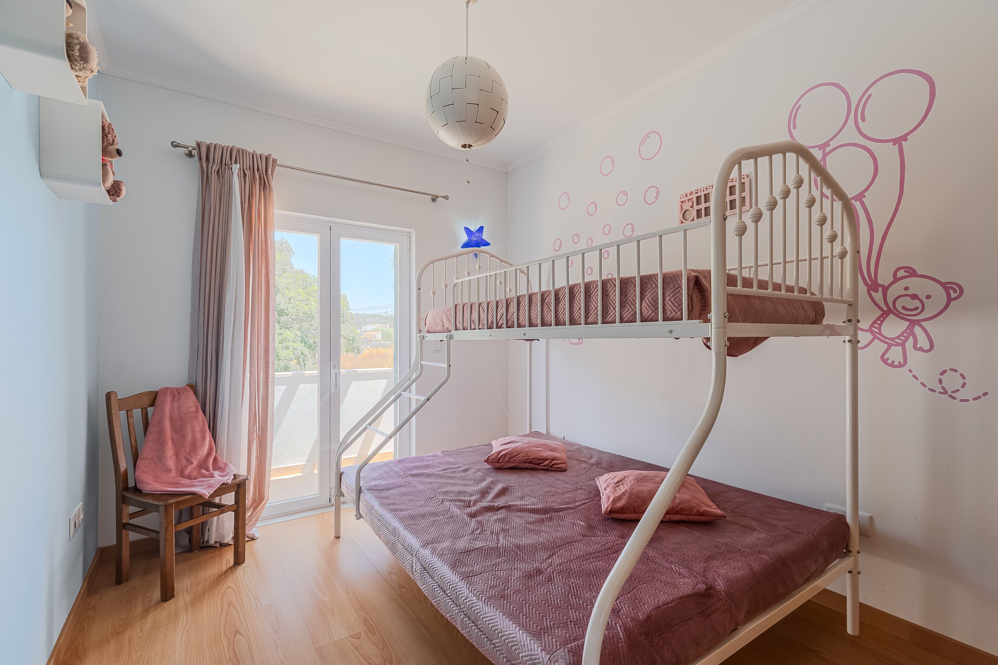 A bunk bed room with a window, a chair, and a teddy bear on the shelf.