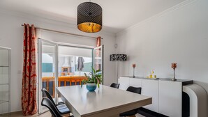 Un espace repas moderne avec une table blanche, des chaises noires, une plante en pot et un luminaire suspendu.