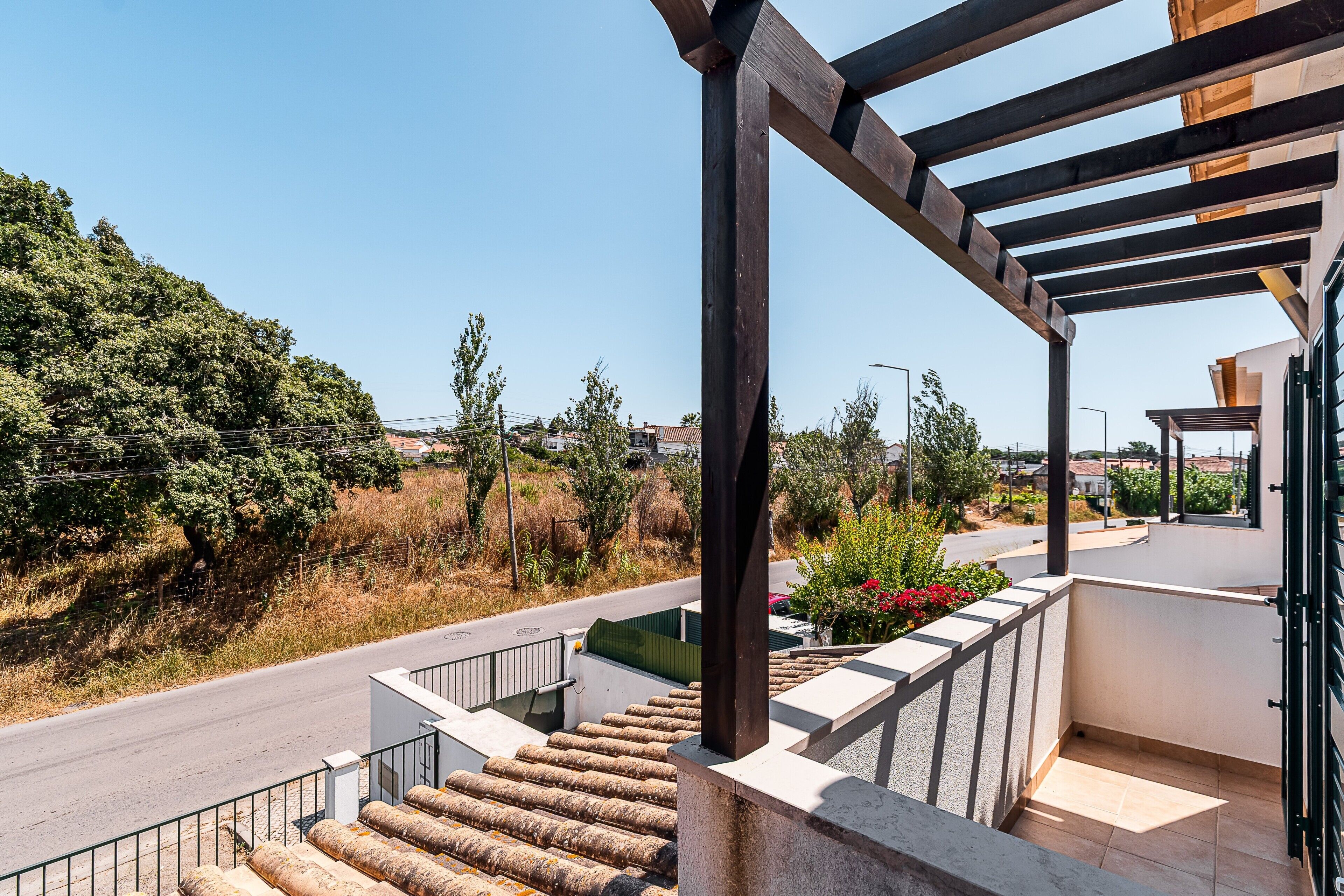Ein Wohnhaus mit Balkon, Treppe und Blick auf eine Straße und Grünflächen.
