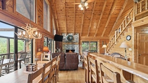 A spacious wooden interior with a fireplace, wooden furniture, and large windows.