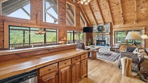 A spacious cabin with a wooden interior, large windows, a stone fireplace, and a ceiling fan.