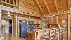 A wooden cabin interior with a kitchen, bar area, and high ceilings.