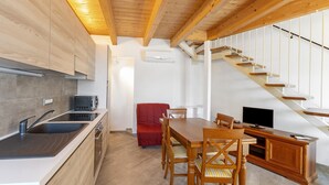 Une cuisine moderne avec un plafond en bois, un coin repas avec une table et des chaises en bois, et un escalier menant à un niveau supérieur.
