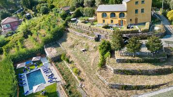 An aerial view of a residential area with a swimming pool, a yellow building, and surrounding greenery.