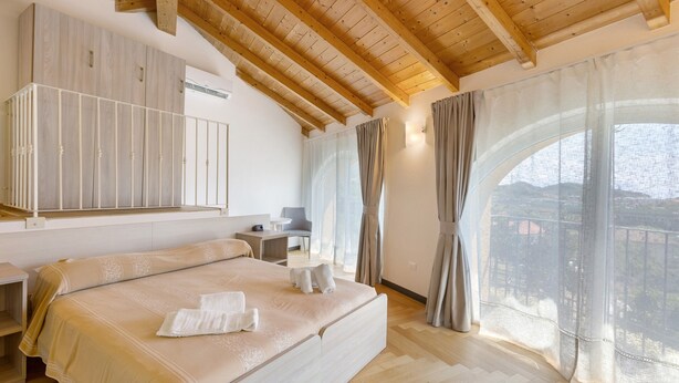 Une chambre à coucher avec un grand lit, un bureau, une chaise et une vue sur l’extérieur par une fenêtre.
