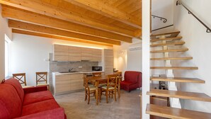 Une cuisine moderne avec des meubles en bois, un coin repas avec une table et des chaises en bois, un canapé rouge et un escalier en bois.