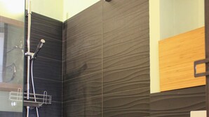 A bathroom with dark tiled walls, a shower with a handheld hose, and a white toilet.