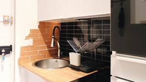A kitchen with a stainless steel sink, a dish rack, and a white cabinet.