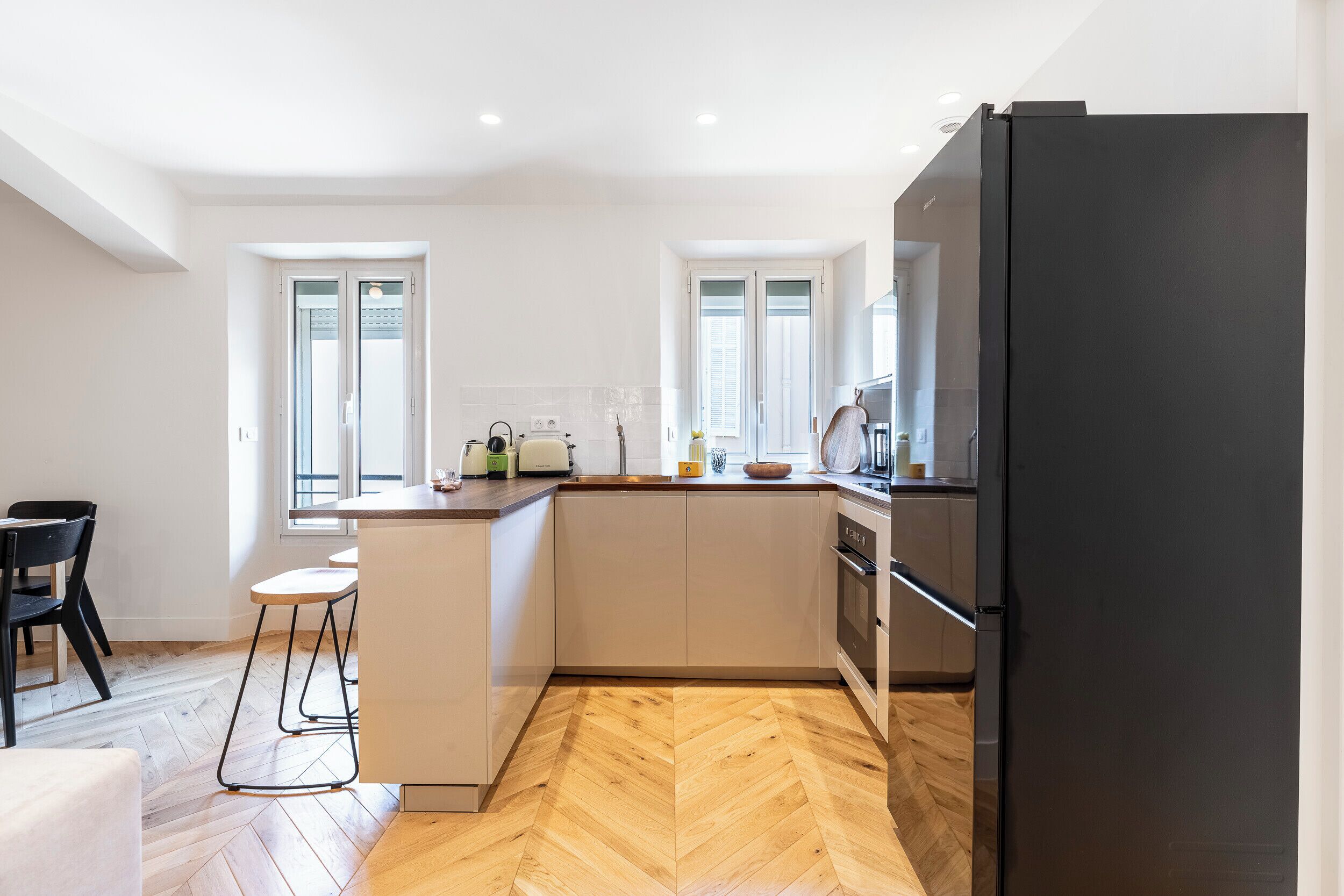 A modern kitchen with white cabinetry, a black refrigerator, and a herringbone wood floor.