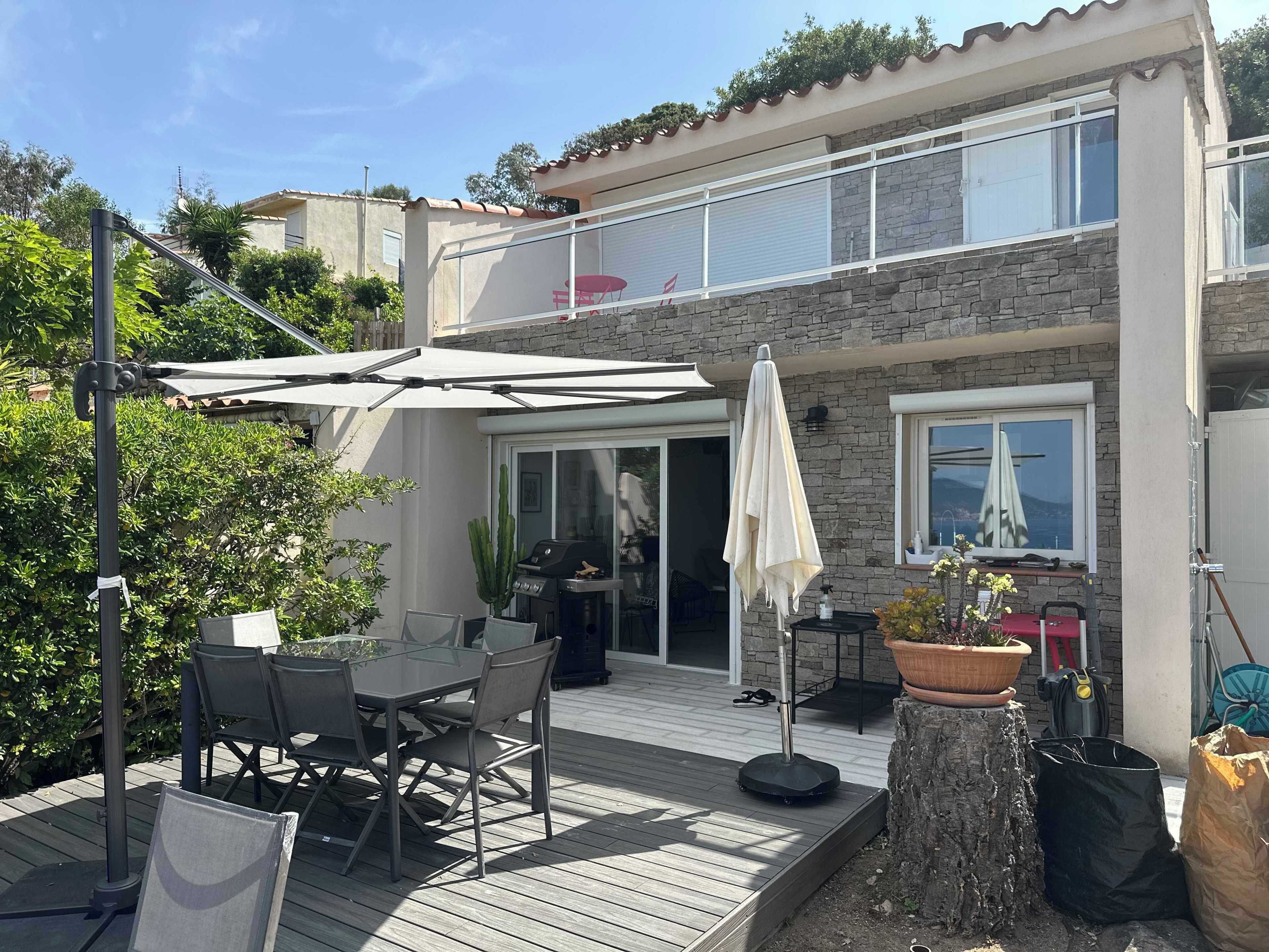 Une maison à deux étages dotée d’un patio comprenant une table et des chaises, un barbecue et une plante en pot.