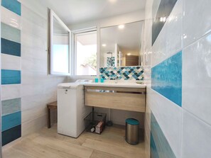 Un baño compacto con lavadora pequeña, un lavabo con espejo y salpicadero de azulejos.