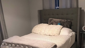 A bed with a grey upholstered headboard, a fluffy white blanket, and a matching pillow.