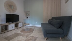 Una sala de estar moderna con un sofá gris, un televisor de pantalla plana sobre un mueble de madera, una pequeña mesa redonda y un espejo decorativo en la pared.