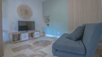 A living room with a grey sofa, a TV on a wooden stand, a woven stool, and a decorative wall piece.