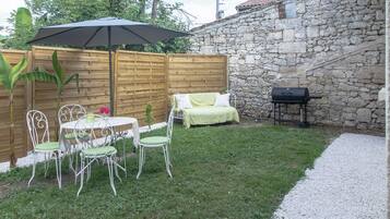 Een terras met een tafel, stoelen, een houten schutting, een stenen muur en een barbecue.
