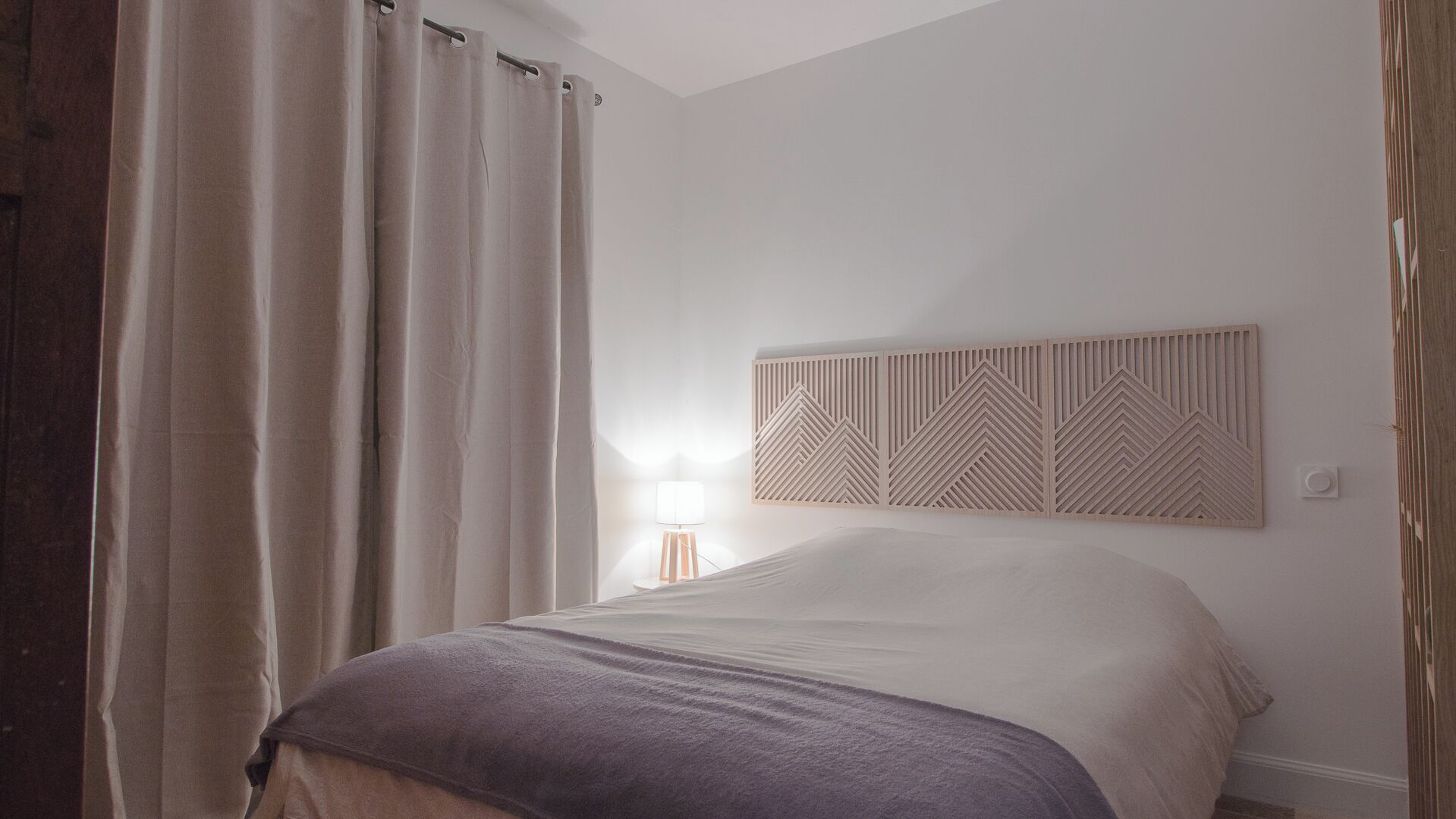 Een slaapkamer met een bed, gordijnen, een bedlamp en een decoratief hoofdeinde.